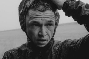 Man in raincoat, serious expression. Matt Johnson.