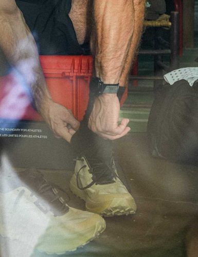 Person tying Norda 055 shoes in reflective setting.