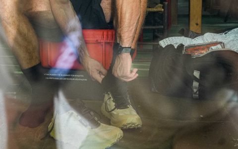 Person tying Norda 055 shoes in reflective setting.